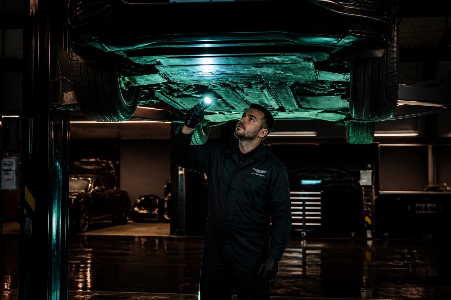 Workshop technician performing a multi-point inspection underneath a premium SUV on a lift